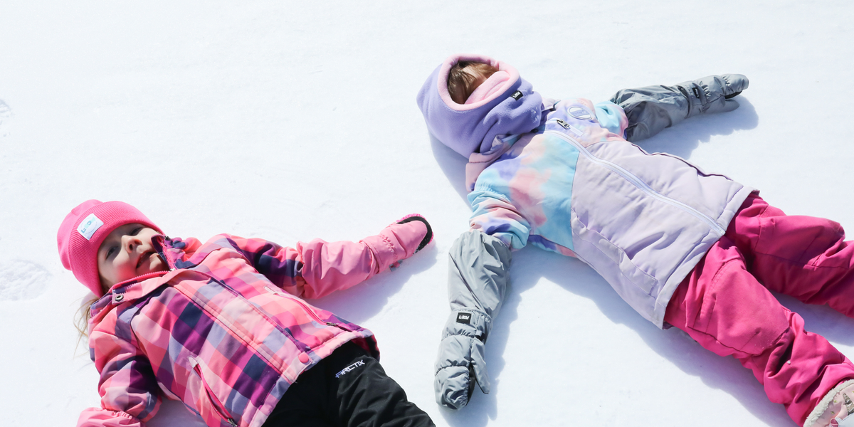 Two children making snow angels in L-Bow kids mittens and a Long Neck fleece gaiter